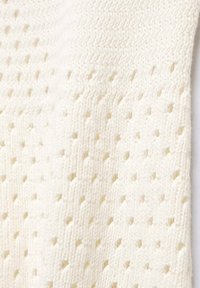 Neulottu valkoinen kangas, jossa on teksturoitu kuvio avoimilla reijillä ja vinoviivoilla, luoden hengittävän ja kevyen ilmeen.