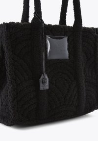 Zwarte draagtas van gestructureerd fleece-materiaal, met een glanzend zwart logo-label, een patroon op de oppervlakte en dubbele handvatten.