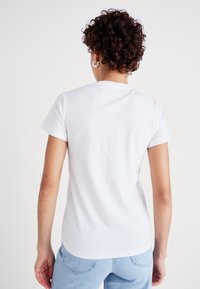 Vit bomull t-shirt med kort ärm, rundad halsringning och en något böjd nederkant bak. Slät textur, utan mönster eller dekorationer.