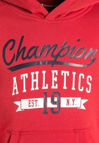 Czerwona bluza z kapturem z przodu z grafiką z napisem "Champion" czarną czcionką, "ATHLETICS" białą oraz "EST. 19 N.Y." w białych literach. Miękka w dotyku.