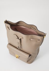 Borsa a secchiello in pelle beige con parte superiore scallop, tasca anteriore con patta magnetica e fodera rosa. Presenta una chiusura con lacci e hardware in tonalità oro.