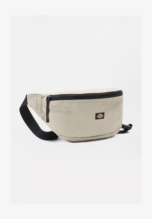 Beige kangastusfanny pakki musta vetoketjulla, säädettävällä hihnalla ja pienellä logotarralla, jolla on kaareva muoto ja sileä pinta.
