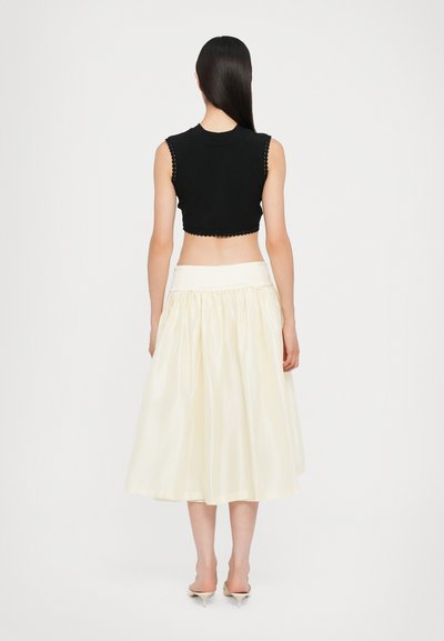 Top negro corto con bordes en forma de escallón, combinado con una falda crema de talle alto y plisada, que resalta una textura suave y brillante.
