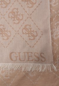 Svetlo bež šal z diskretno vzorčasto teksturo, ki vsebuje prepletene črke G, označen z "GUESS" in končan z resicami.
