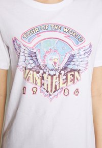 Bílý bavlněný tričko s barevným grafickým motivem zobrazujícím orla, zeměkouli a text "Tour of the World Van Halen 1984."