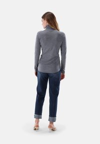 Graues Langarm-Turtleneck-Oberteil mit figurbetontem Design, kombiniert mit hochgekrempelten blauen Jeans. Das Modell trägt beige Absätze.