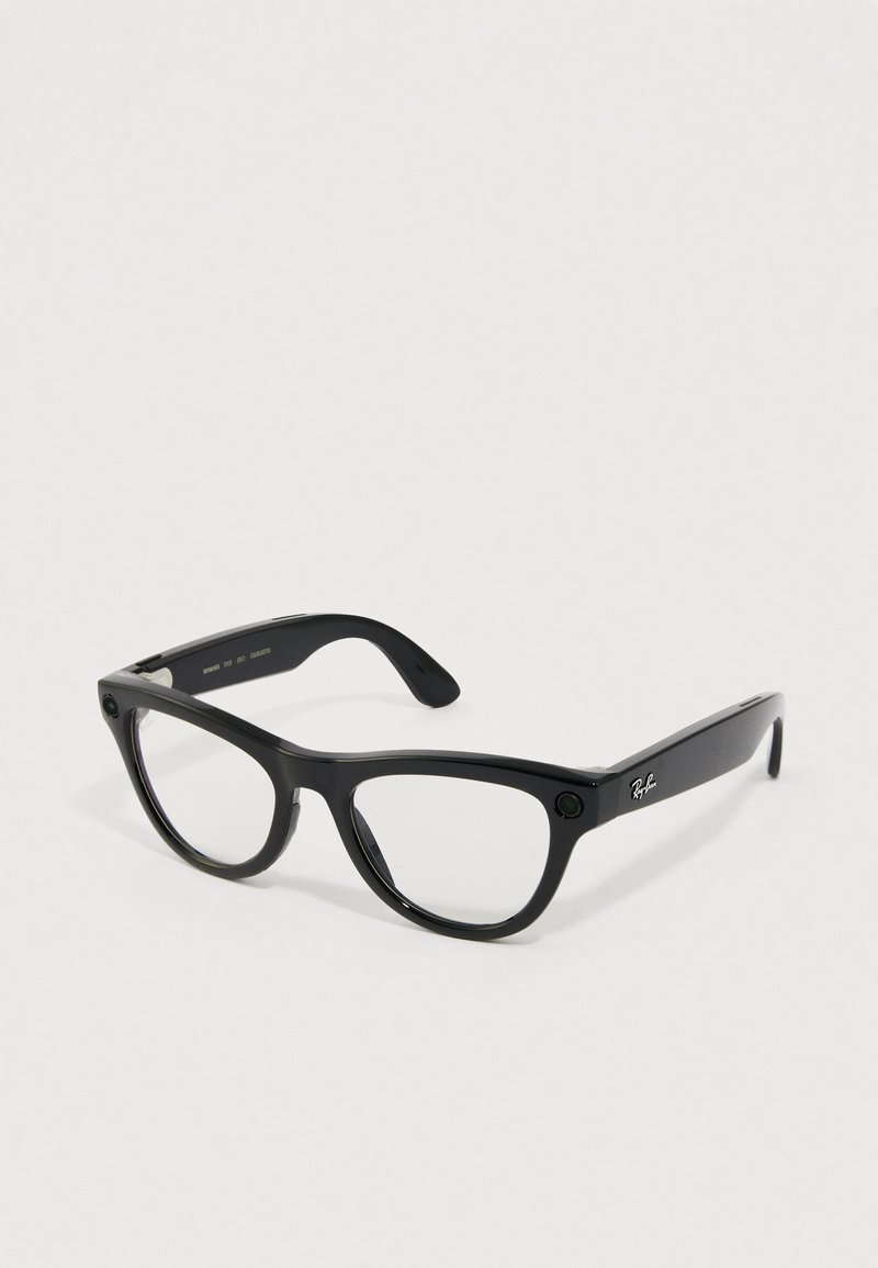 Gafas Ray-Ban negras rectangulares con lentes transparentes descansando sobre una superficie clara, mostrando el logotipo plateado en la patilla.