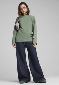 Žalias ilgomis rankovėmis viršus, tamsūs plačiomis kojomis džinsai ir žali batai. Aksesuarai: sidabrinės saulės akiniai ir sidabrinė pečių rankinė.