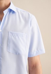 Camicia azzurro chiaro a maniche corte realizzata in tessuto liscio, con colletto a punta e una piccola tasca sul petto con apertura piatta.