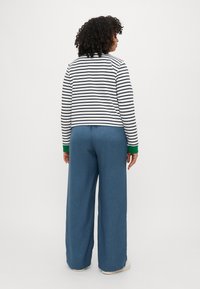 Top a maniche lunghe a righe in navy e bianco con accenti verdi, abbinato a pantaloni larghi blu. Tessuto morbido e vestibilità rilassata.