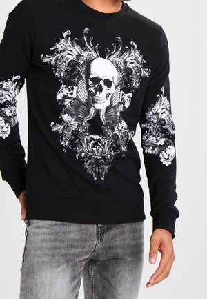 Sudadera negra de mangas largas con un diseño de calavera blanca rodeada de patrones florales y ornamentados; puños y dobladillo acanalados.