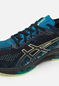 Scarpa da corsa nero e blu con tomaia in mesh strutturato, dettagli gialli e suola imbottita progettata per supporto e comfort.