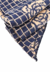 Piletta di lana beige e blu marino con motivo a griglia, caratterizzata da una texture morbida. I bordi sono rifiniti con cuciture precise, mostrando una piegatura triangolare.