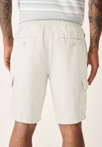 Light gray linen cargo shorts with an elastic waistband, two side pockets, and two rear buttoned pockets. Casual and relaxed fit.