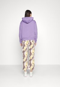Fioletowa bluza z luźnym krojem, zestawiona z wzorzystymi spodniami w kremowych, brązowych i żółtych odcieniach o szerokich nogawkach. Białe trampki dopełniają zestaw.