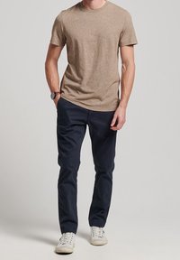 Hnědé triko s krátkým rukávem v kombinaci s námořnickými chinos kalhotami a bílými teniskami. Jednoduchý design, hladká textura a neutrální barevná paleta.