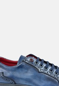 Zapato de cuero azul con una textura suave, con detalles de brogue, cordones redondos, interior rojo y ojales en contraste.