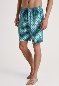 Zwemshorts met een geometrisch patroon in teal en marineblauw, gemaakt van lichte stof met een elastische tailleband en een trekkoordsluiting.