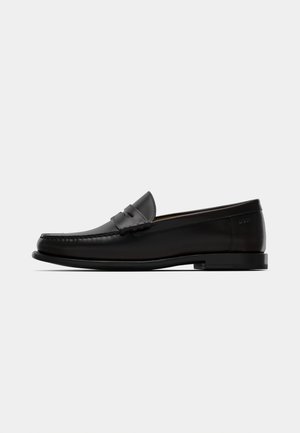 Black leather loafer with a rounded toe, decorative stitching, and a flat rubber sole. Features a subtle brand logo on the heel.