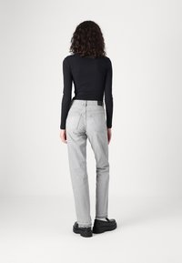 Lys grå jeans med rett passform, fem-lomme design og frynset kanter, sammen med en svart ribbestrikket langermet topp og klumpete svarte sko.