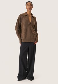 Brun strikket sweater med krave og halvknaplukning, parret med løse sorte bukser, der fremhæver en afslappet pasform og blød tekstur.