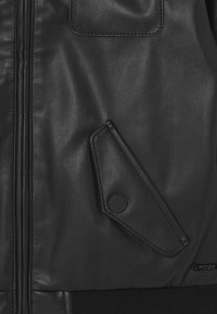 Zwarte leren jack met een gladde textuur, voorzien van een zijrits en een diamantvormige flapzak met een drukknoopsluiting.