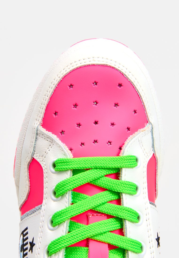 Białe sneakersy z różowymi akcentami i zielonymi sznurówkami. Posiadają perforacje w kształcie gwiazdek oraz gładką teksturę. Nowoczesny, sportowy design.