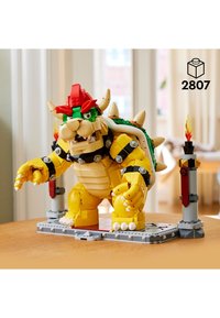 LEGO model of Bowser, featuring a yellow body, red and green accents, spiked shell, and arm movements. Includes two torches on the base.