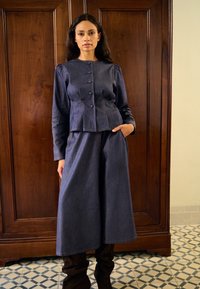 Jachetă din denim închis la culoare, cu închidere cu nasturi și mâneci bufante, asortată cu pantaloni cu picioare largi. Textură netedă cu detalii de cusături contrastante.