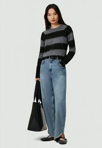 Sweater riscado em preto e cinza, jeans de sarja de lavagem clara de corte largo com bainha desfiada, bolsa tote preta e sapatos slip-on pretos com tachas.