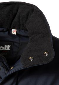 Collar de chaqueta azul marino con forro de forro polar negro, broches de latón y una etiqueta con la letra "L". Presenta una textura exterior suave.