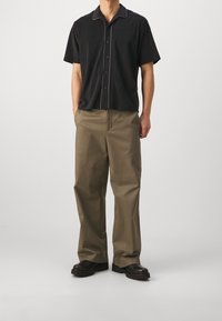 Musta lyhythihainen paita, jossa on kontrastivärinen kaulus, napit edessä, yhdistettyinä löysiin oliivinvihreisiin housuihin ja mustiin paksupohjaisiin kenkiin.