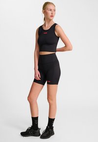 Svart kort sporttopp och höga midjeshorts med röda logodetaljer. Tyget verkar vara stretchigt med en slät yta.