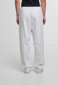 Light gray sweatpants with an elastic waistband, featuring a relaxed fit, dual side seams, and ribbed ankle cuffs. Smooth texture.
