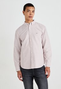 Striped button-up shirt in light pink and white, made from woven fabric, with a pointed collar and long sleeves. Subtle logo on chest.