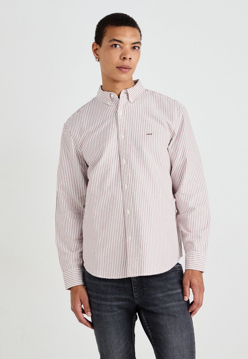 Striped button-up shirt in light pink and white, made from woven fabric, with a pointed collar and long sleeves. Subtle logo on chest.