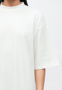 Hvit bomulls-t-skjorte med høy hals og korte ermer. Myk tekstur, løs passform og minimalistisk design uten mønstre eller aksenter.