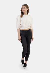 Krémová, stažená mikina s nafouknutými rukávy, kombinovaná s černými slim-fit džíny a černými teniskami s bílými podrážkami.