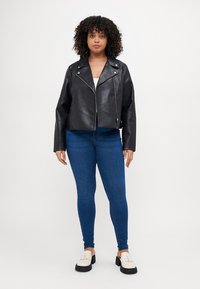Black leather cropped biker jacket with a zip closure and silver hardware, worn over a light top and paired with blue skinny jeans.