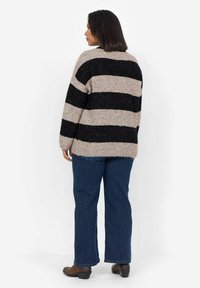 Striped sweater in beige and black wool blend, featuring a loose fit, round neckline, and dropped shoulders, paired with blue denim jeans.