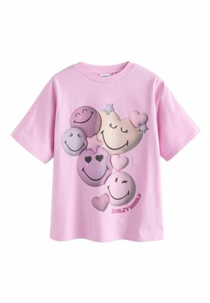 Vaaleanpunainen puuvillati-paita, jossa on erilaisia hymiökuvioita purppuran sävyissä, mukaan lukien sydämiä ja tähtiä, sekä "SMILEY WORLD" -teksti alaosassa.