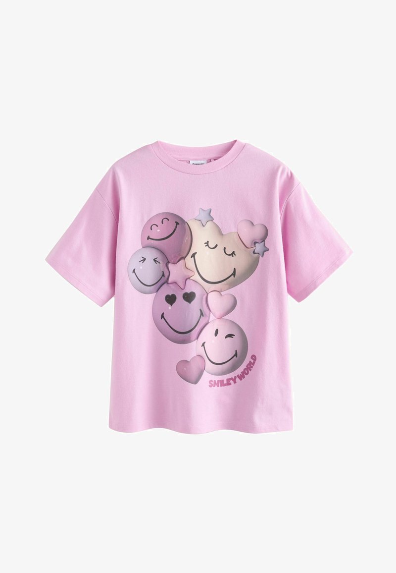 Rozā kokvilnas T-kreklā ir dažādi smaidošu seju grafiki purpura toņos, tostarp sirdis un zvaigznes, ar tekstu "SMILEY WORLD" apakšā.
