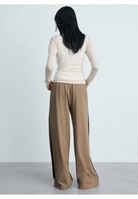 Haut beige à manches longues et pantalon beige à jambes larges avec fentes latérales, en tissu doux. Design uni, sans motifs ni éléments métalliques visibles.