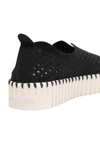 Schwarzer perforierter Schuh mit einem strukturierten synthetischen Obermaterial, ausgestattet mit einer weißen Plattformsohle mit vertikalen Rillen und einer erhöhten Rückenschlaufe.
