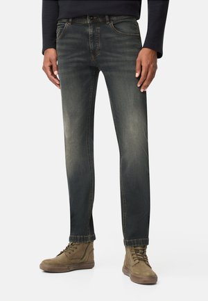 Dunkelblaue Jeans mit einem ausgebleichten Finish, geradem Beinansatz, Fünf-Taschen-Design und braunen Akzentnähten; getragen mit braunen Schnürstiefeln.