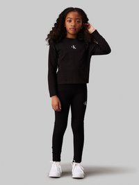 Svart långärmad topp och leggings-set med en vit "CK"-logotyp. Slät bomullsmaterial, figursydd form, kombinerat med vita sneakers.