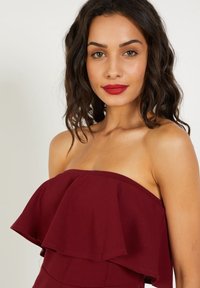 Vestido burdeos sin mangas con detalle de volantes en el escote, confeccionado en una tela suave con una silueta ajustada.