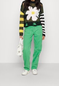 Pull en tricot avec un motif floral, présentant des rayures noires et jaunes ; associé à un pantalon vert et un sac à main blanc.