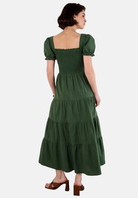 Grünes, gestuftes Maxikleid mit gerafftem Oberteil, kurzen Puffärmeln und einem quadratischen Rückenausschnitt. Hergestellt aus leichtem Stoff, der ein fließendes Design aufweist.
