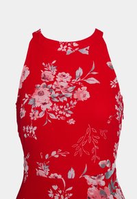 Robe rouge sans manches avec un col montant, présentant un imprimé floral rose et gris ainsi que des motifs de feuilles.